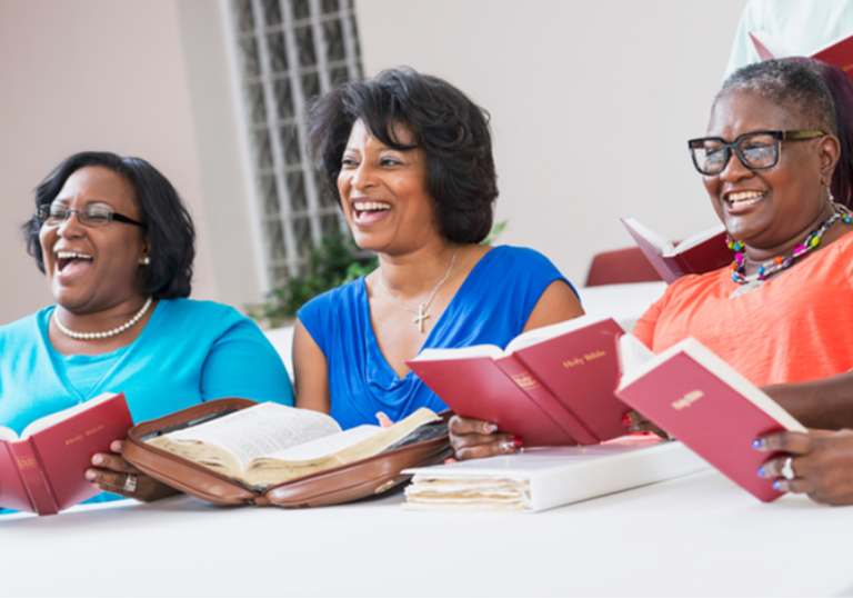 Three smiling women singing with red songbooks