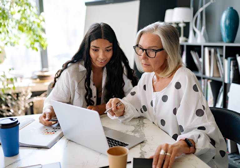 Two women collaborating at laptop in modern office